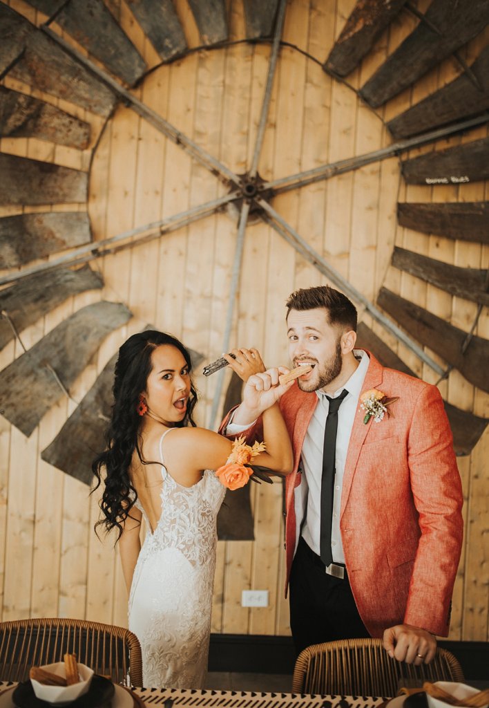 Playful wedding moment with churros at a barn venue.