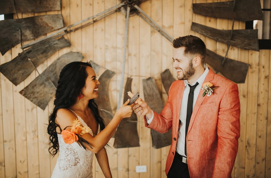 Bride and groom laughing while sharing churros at their reception.