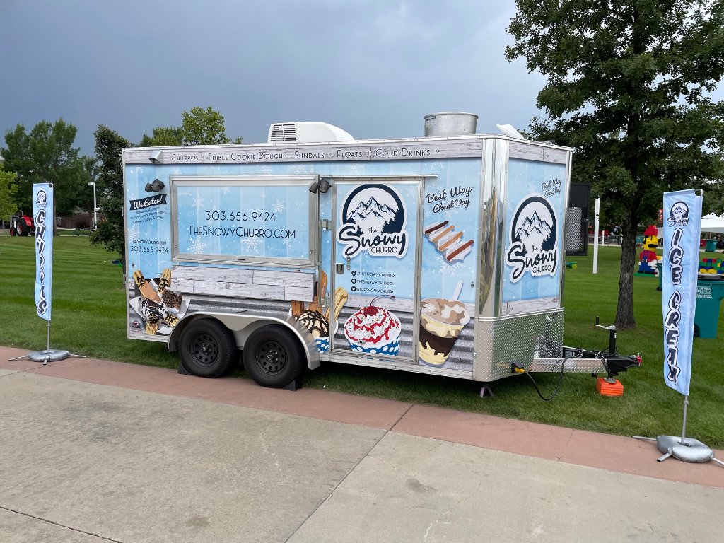 The Snowy Churro trailer at a community event with feather flags and play area.
