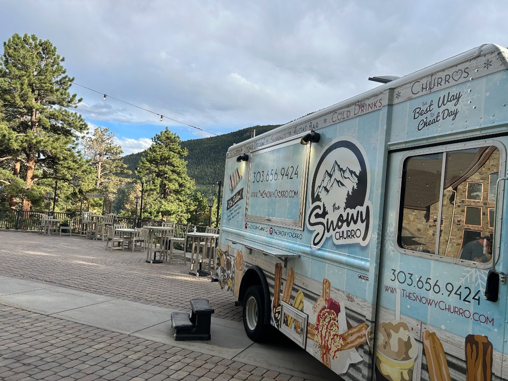 The Snowy Churro truck on a paved patio surrounded by pines.