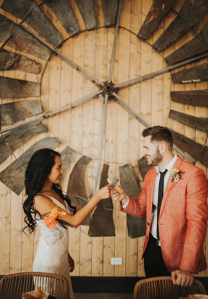 Bride and groom toasting churros in front of a rustic windmill.