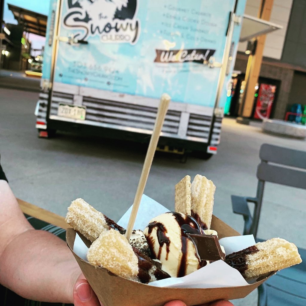 Hand-held churro sundae with ice cream and chocolate in front of The Snowy Churro truck.